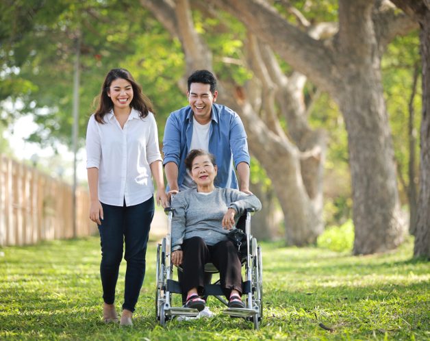 Asian senior woman sitting on the wheelchair with family happy smile face on the green park