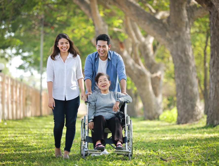 Asian senior woman sitting on the wheelchair with family happy smile face on the green park