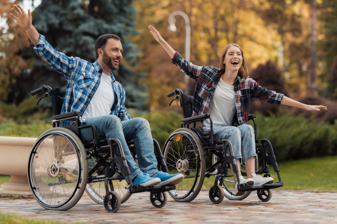 A man and a woman on wheelchairs ride around the park.