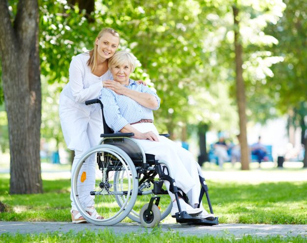 Pretty nurse taking care of senior patient in a wheelchair